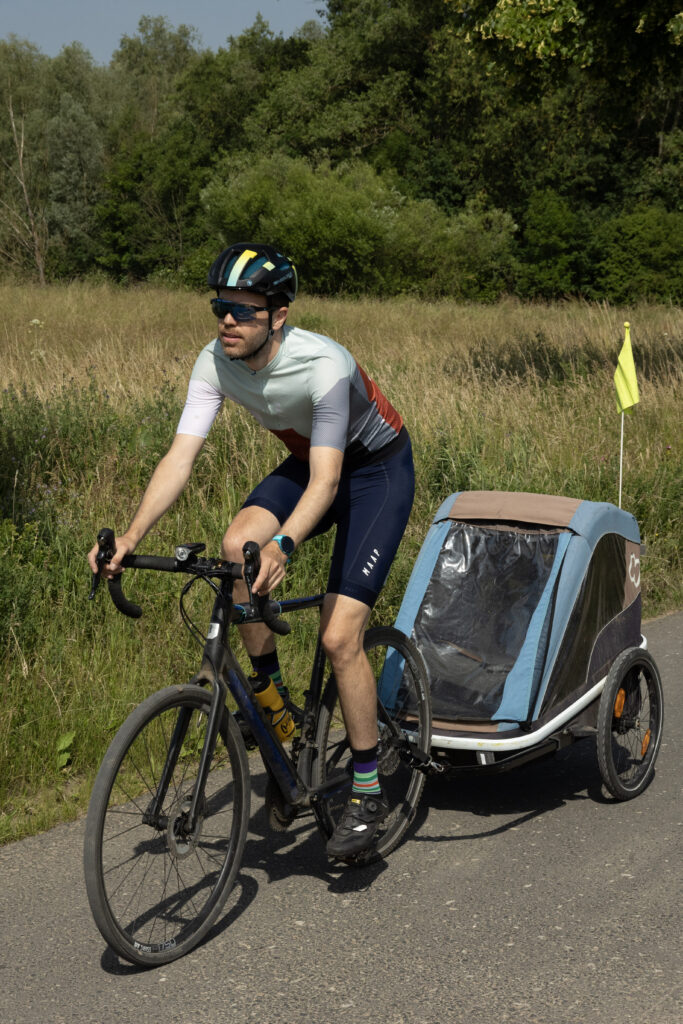 Cyclist with Hamax Avenida Twin bike trailer attached to cross bike flies past from right to left.