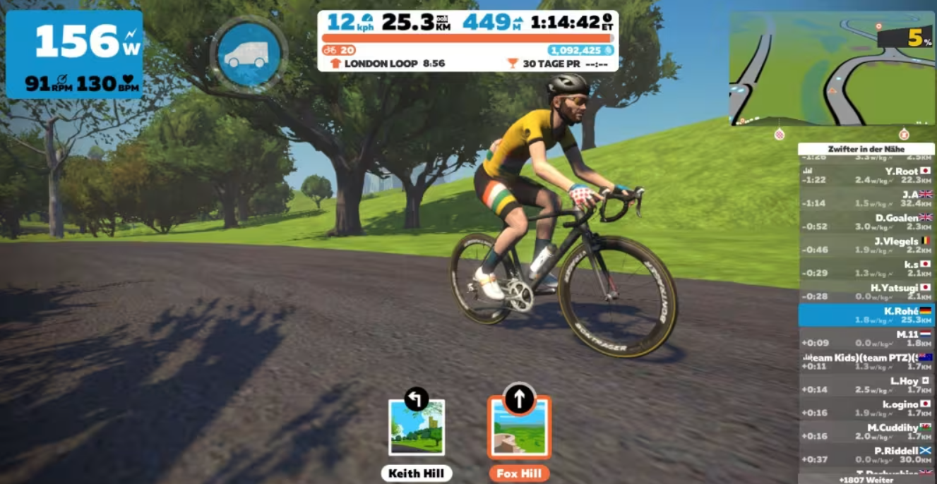 Screenshot from indoor training software Zwift with bearded male cyclist moving up Fox Hill with trees in background