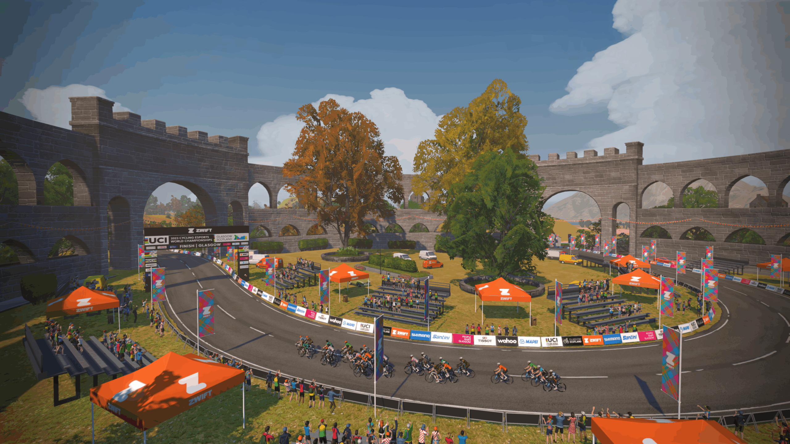 Grou of Zwift riders appraoch the finish line with lots of tents ans spectators around.