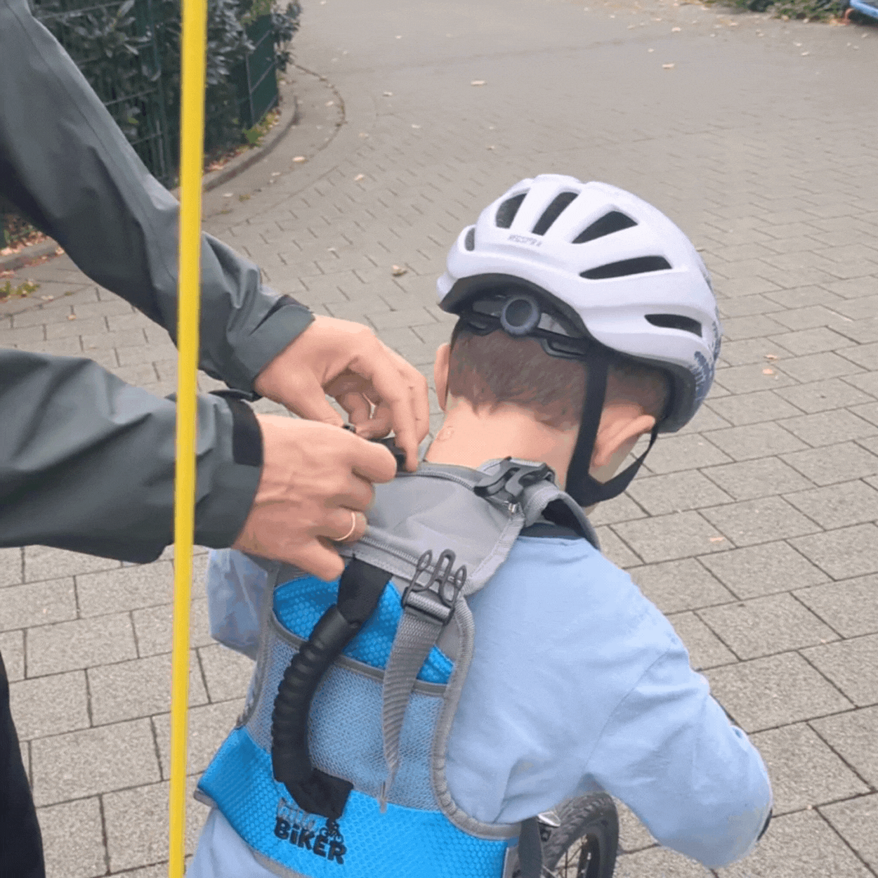 Parent's hands adjust the Little Biker vest worn by a kid on a bike with a helmet