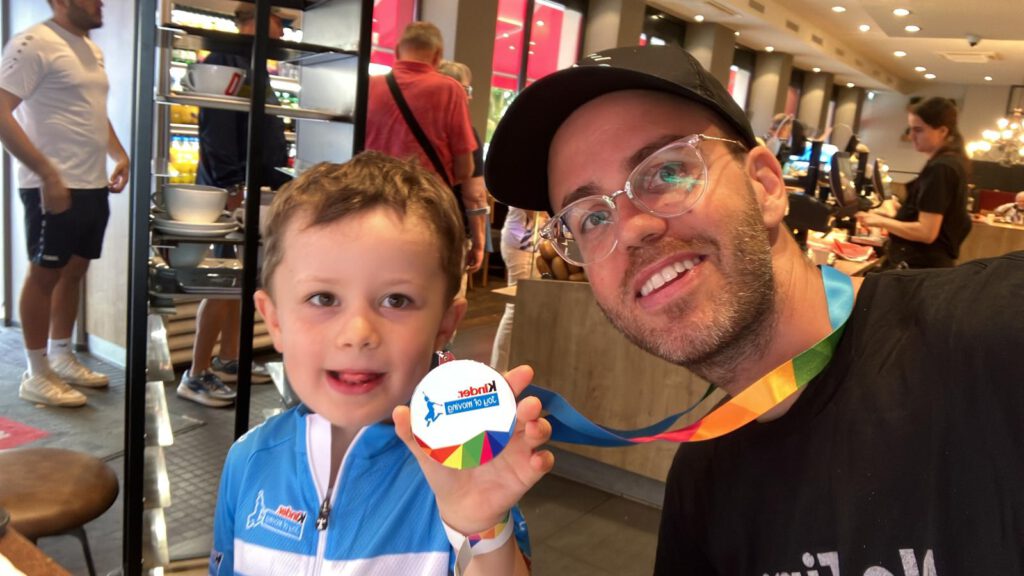 DTour-BadOrb-2026-medal Proud medalist with dad after the Joy of Moving Mini Tour Bike Parade.